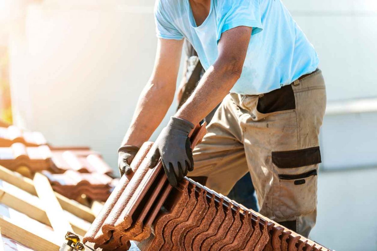 Roofing - construction workers standing on a roof covering it with tiles; professional roof installation