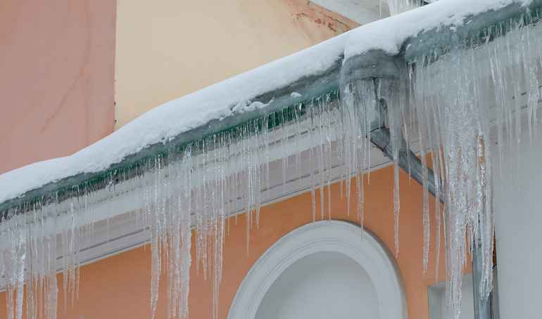 Vintage building icy downpipe and roof with icicles. Cold winter weather concept