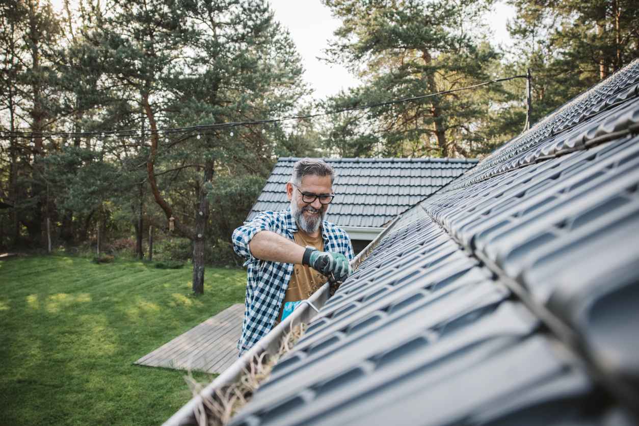 Mature man cleaning leaves from guttering of house.