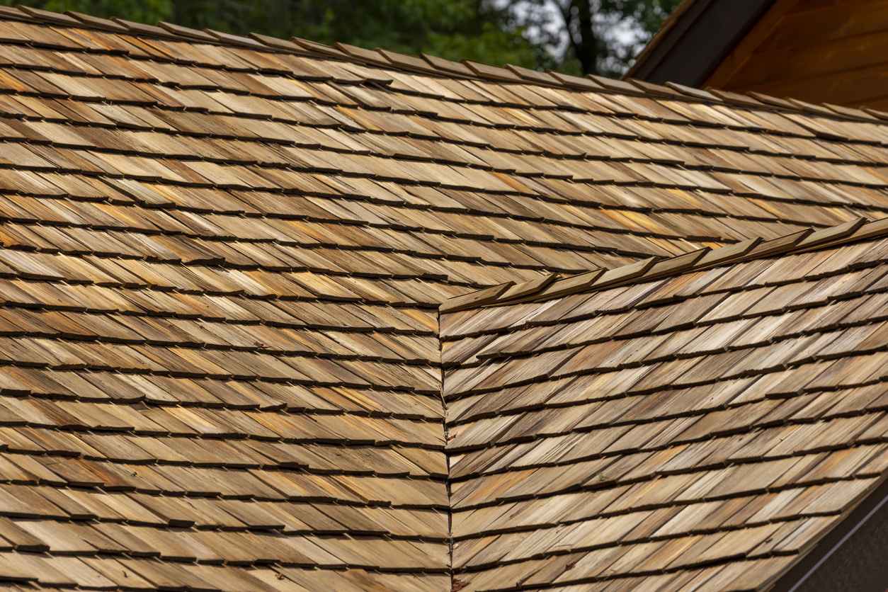 New cedar shingle roof with valley and ridge cap coming together at center of frame