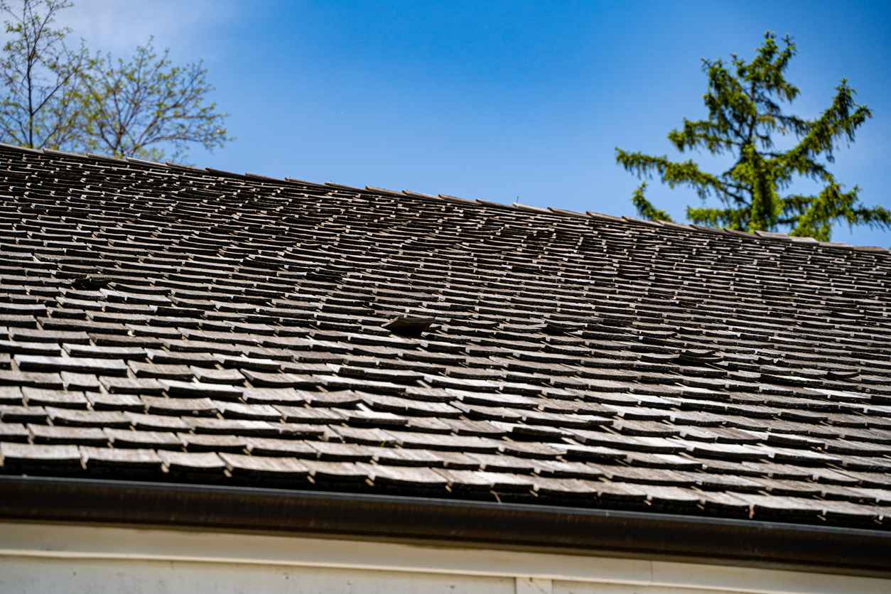 Close up of old and worn wooden shingle roof under blue sky.